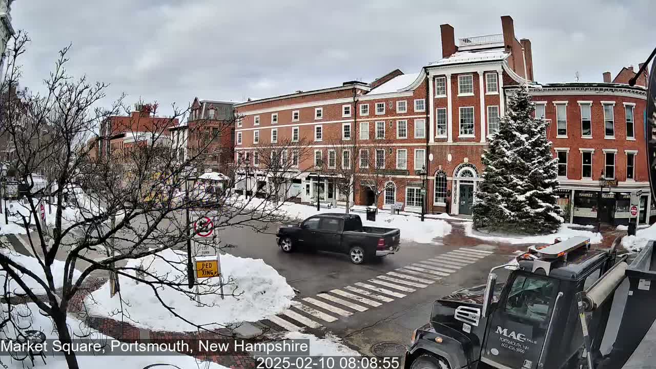 A snow-covered Market Square in Portsmouth, New Hampshire, shows several brick buildings, a dark-colored pickup truck, and a dark-colored dump truck at an intersection.