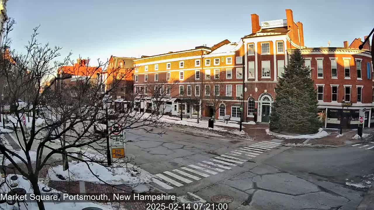 A snow-covered town square with several brick buildings under a clear, bright sky at sunrise.