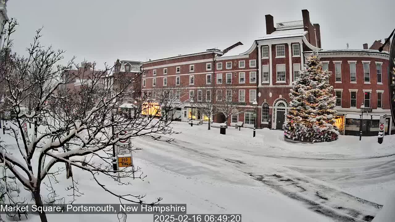 Snow-covered Market Square in Portsmouth, New Hampshire, features brick buildings, a decorated Christmas tree, and bare, snow-laden trees under a gray sky.