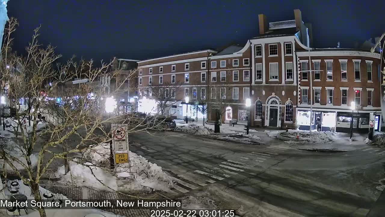 A snow-covered street at night, lined with brick buildings, is illuminated by streetlights.