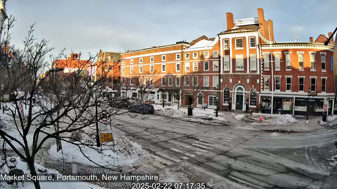 A snow-covered street scene shows brick buildings under a partly sunny sky.