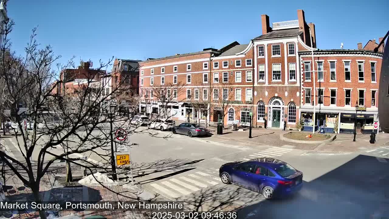 A sunny day in a brick-lined town square with several cars and bare trees.