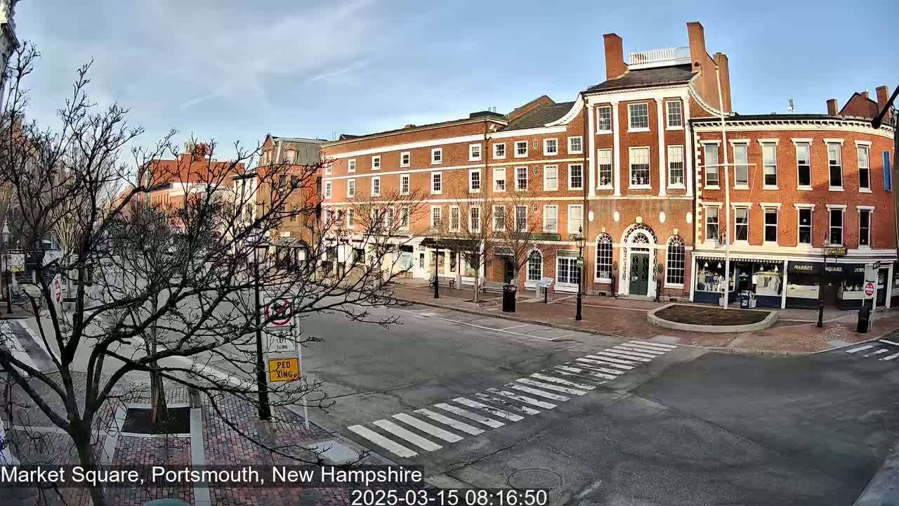 A mostly empty brick-lined town square with several multi-story buildings under a clear, sunny sky.