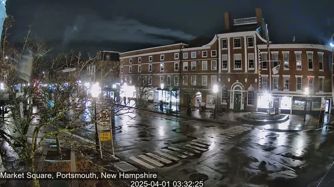 A wet, nighttime street scene shows a brick building and a square with pedestrian crossings.