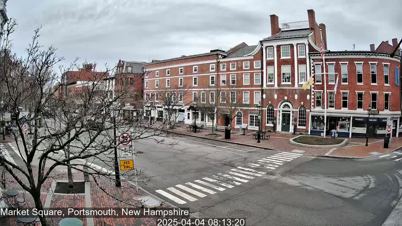 A mostly empty town square with brick buildings and bare trees under an overcast sky.