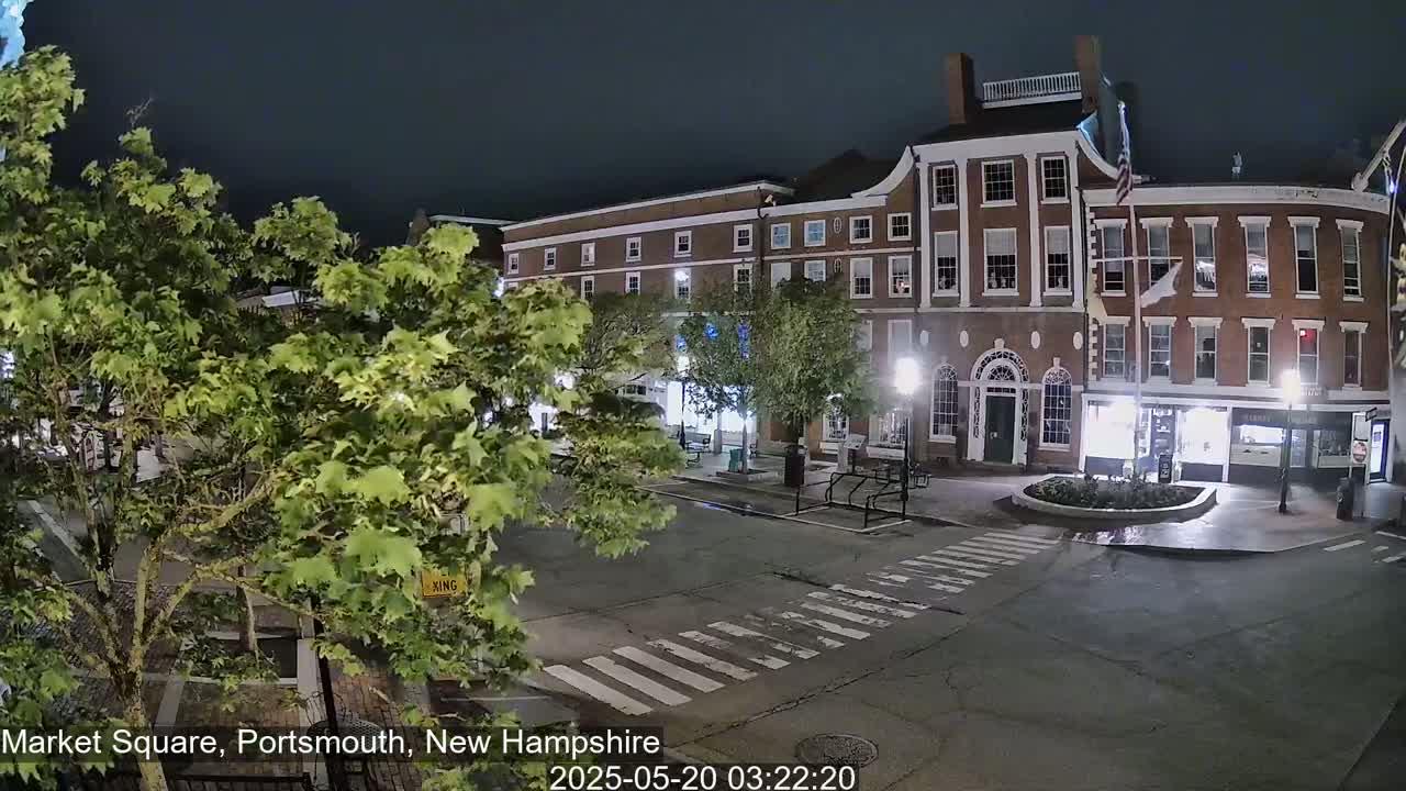 A nighttime view of a brick building and town square, with trees swaying gently in the breeze.