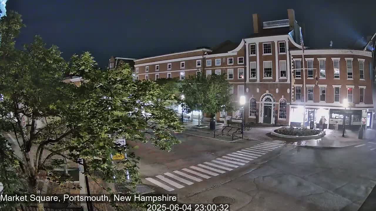 A nighttime view of a brick building and a square with a pedestrian crossing, under a clear sky.