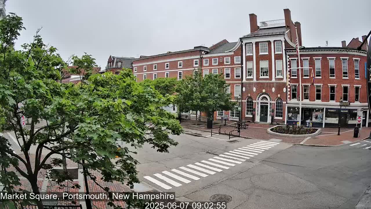 A brick building and a square with a crosswalk are seen on an overcast day.