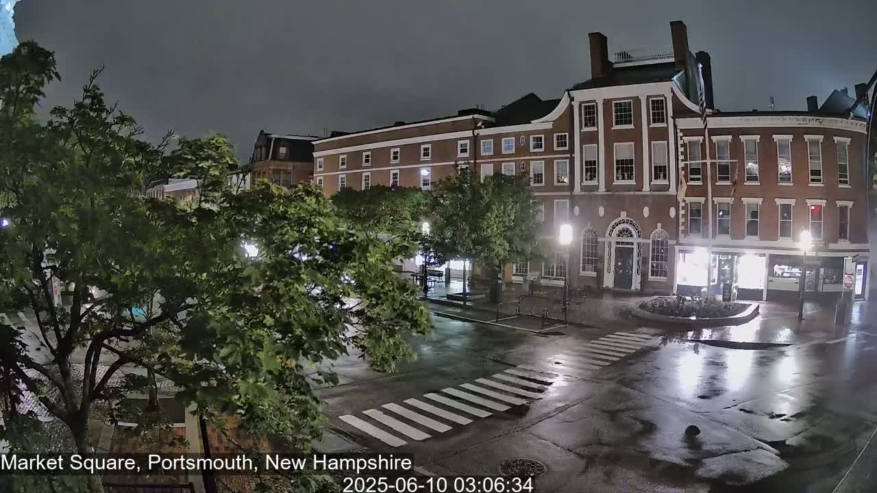 A wet, nighttime street scene shows a brick building and crosswalk under a dark sky.