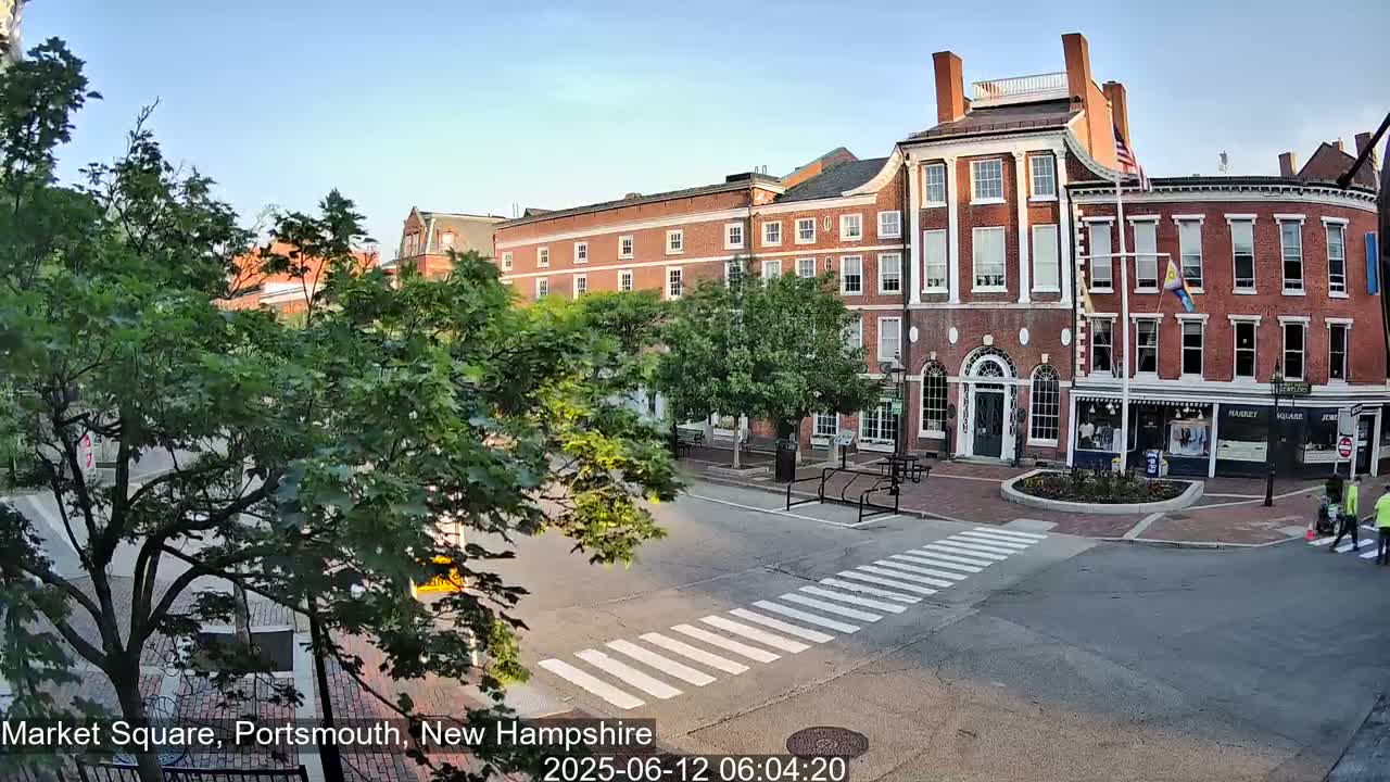 A brick building and street scene on a sunny day, with green trees and a pedestrian crossing.
