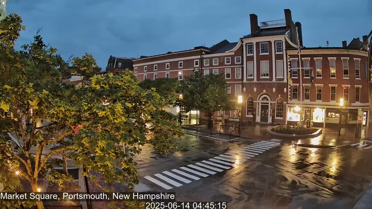 A wet, dark city square at night, with brick buildings and streetlights reflecting in the puddles.