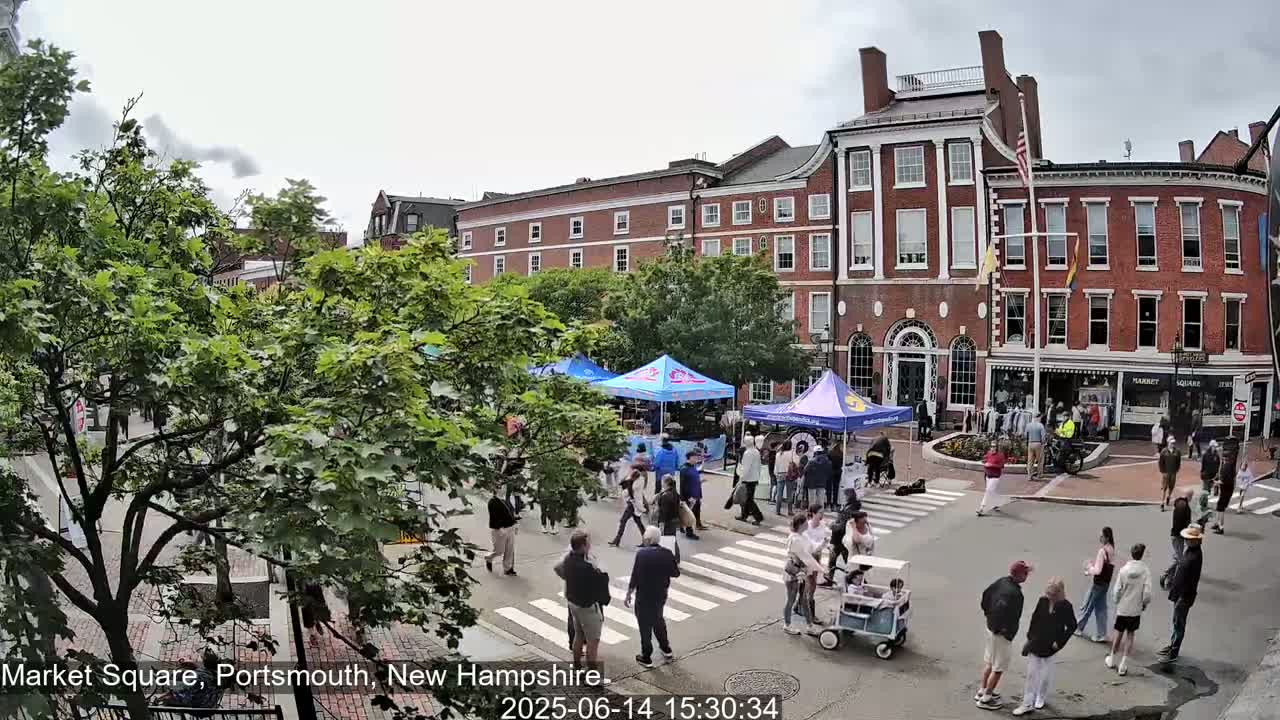 A wet Market Square in Portsmouth, New Hampshire, shows several people crossing a street in front of brick buildings with market stalls set up under canopies.