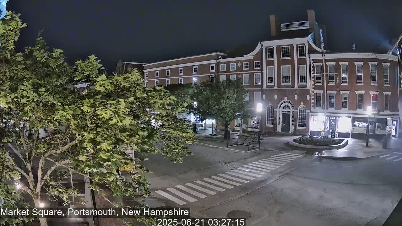A nighttime view of a brick building and town square with crosswalks and trees.