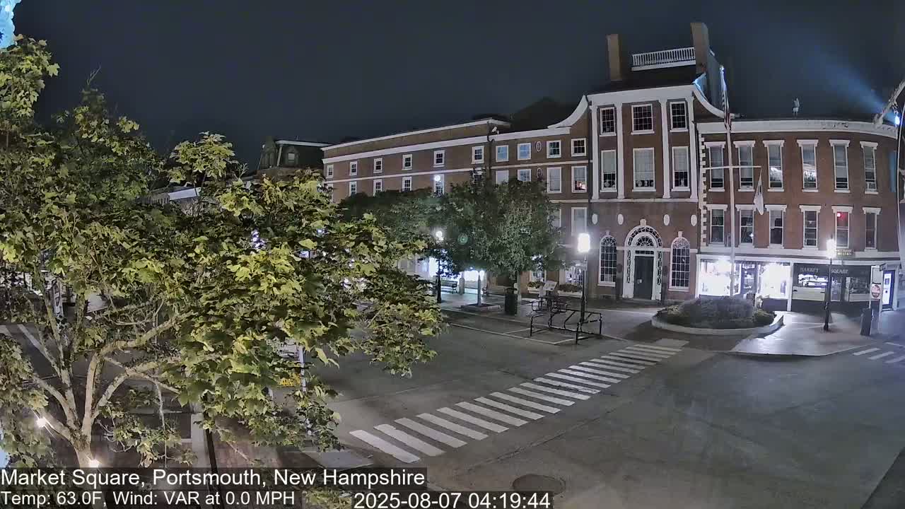 A nighttime view of a brick building and a square, with trees and streetlights illuminating the scene under calm, clear conditions.