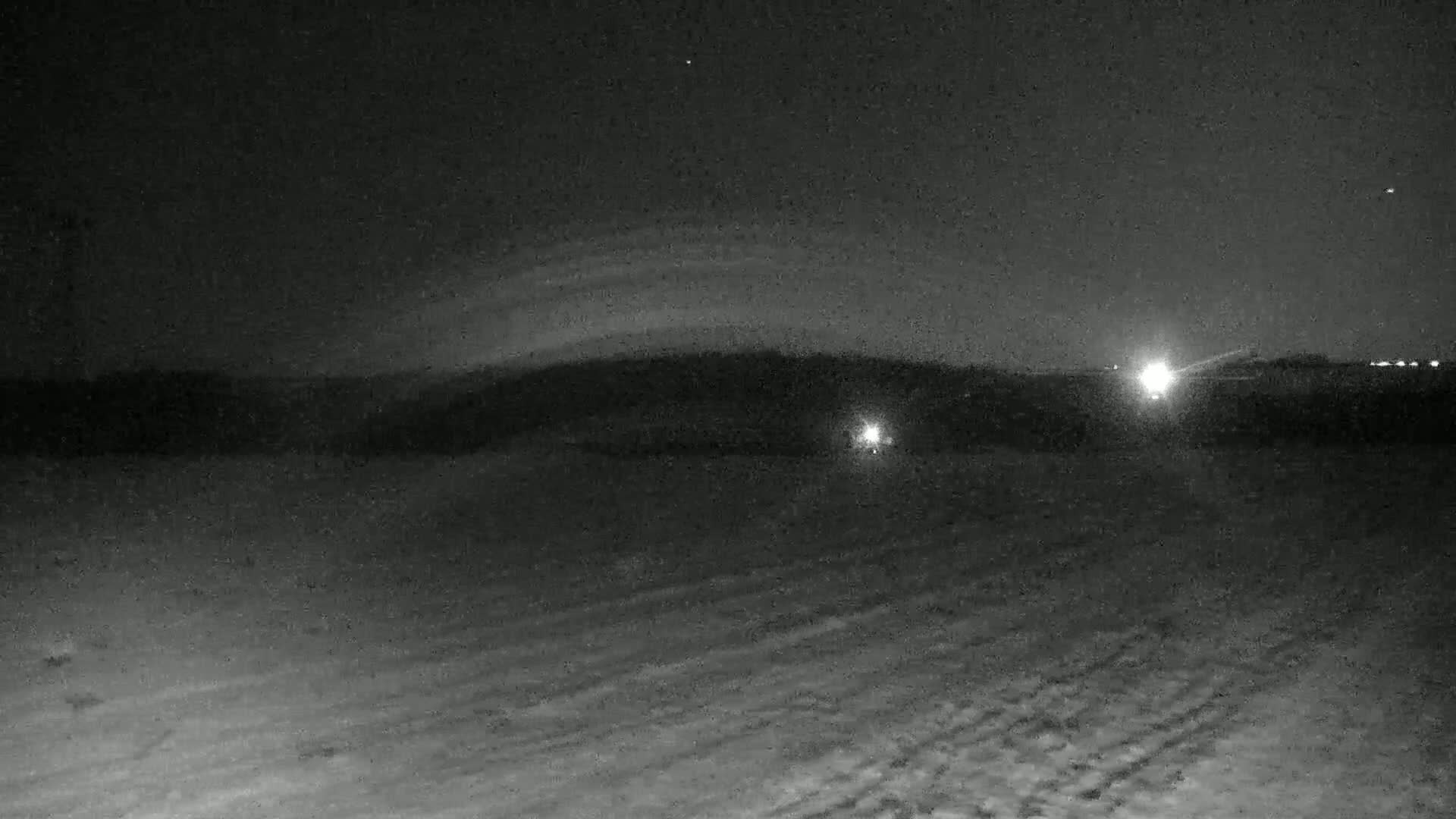 A snow-covered landscape is visible at night under a dark sky with a faint, arched cloud formation and a few distant lights.