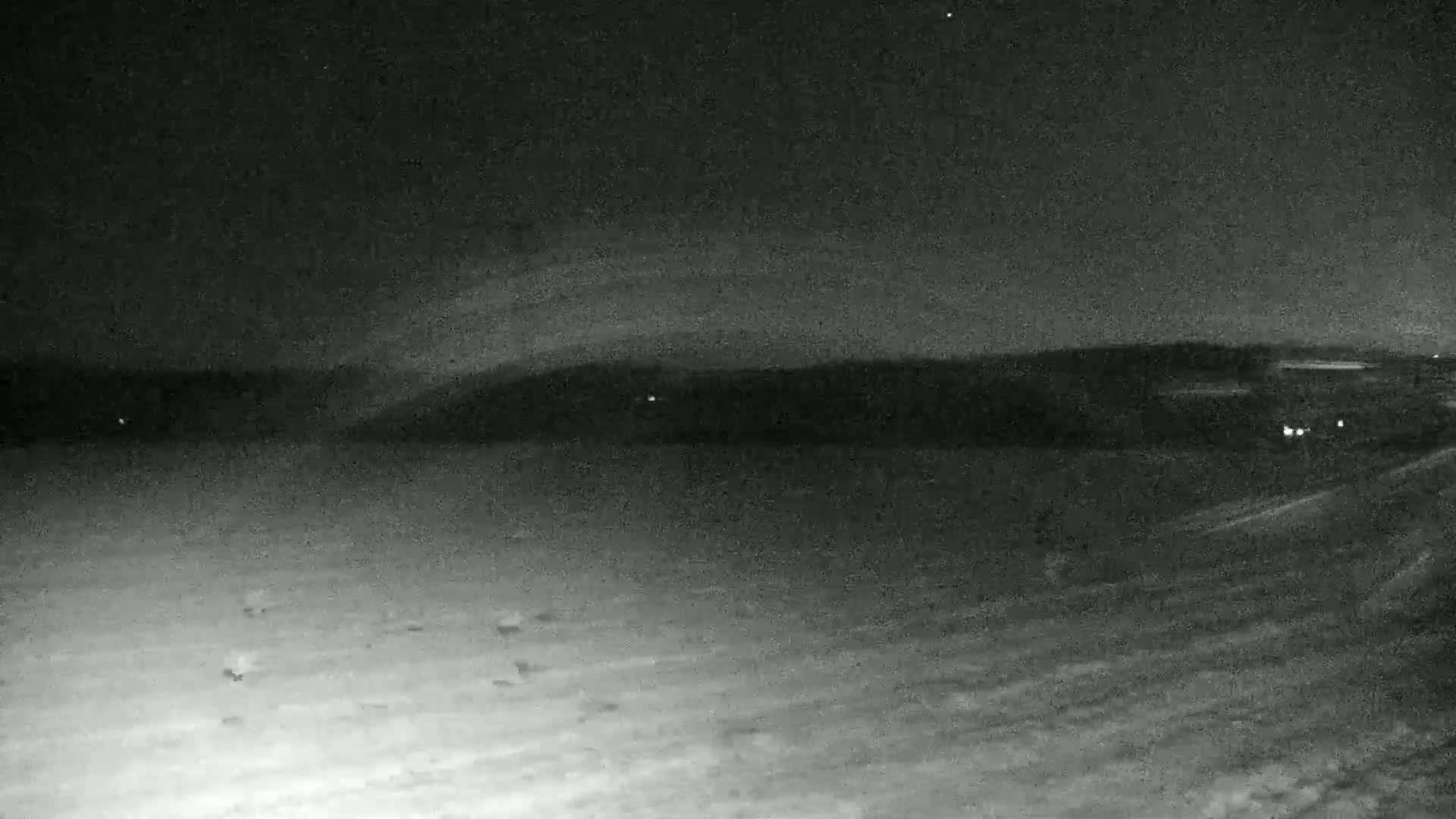 A nighttime, snow-covered landscape shows a dark horizon line with faint lights in the distance.
