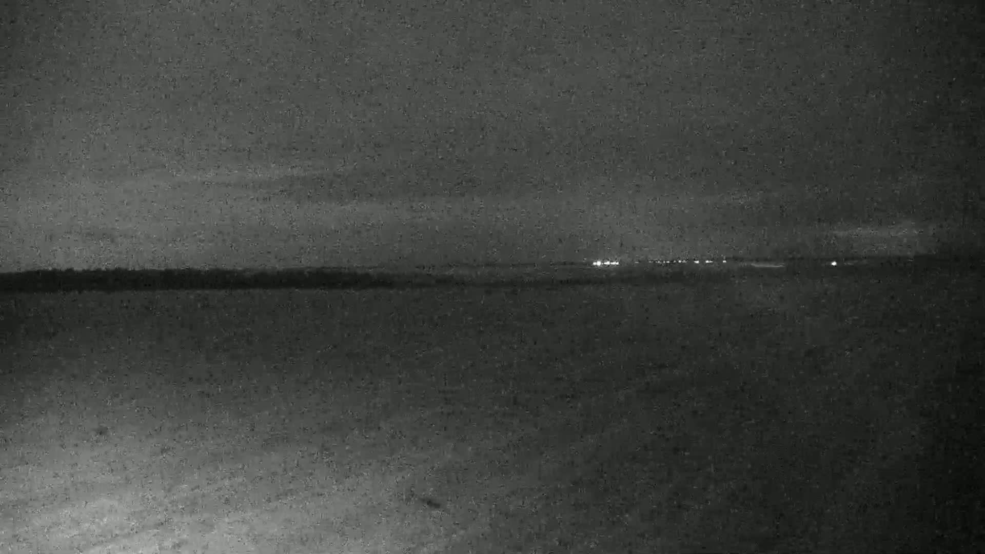 A dark, flat landscape is visible under a night sky, with distant lights faintly illuminating the horizon.