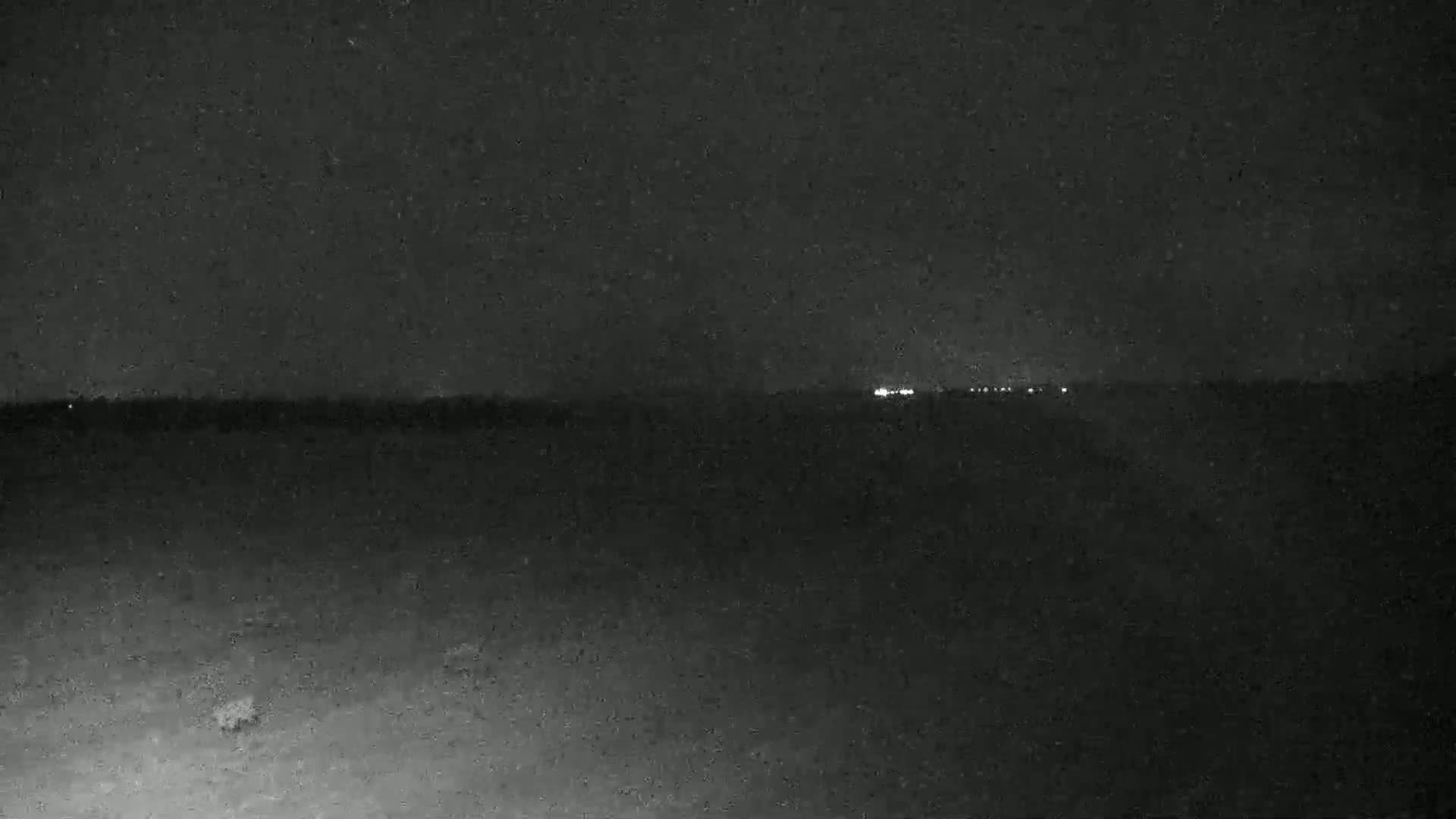 A dark, nighttime landscape shows a distant line of faint lights on the horizon.