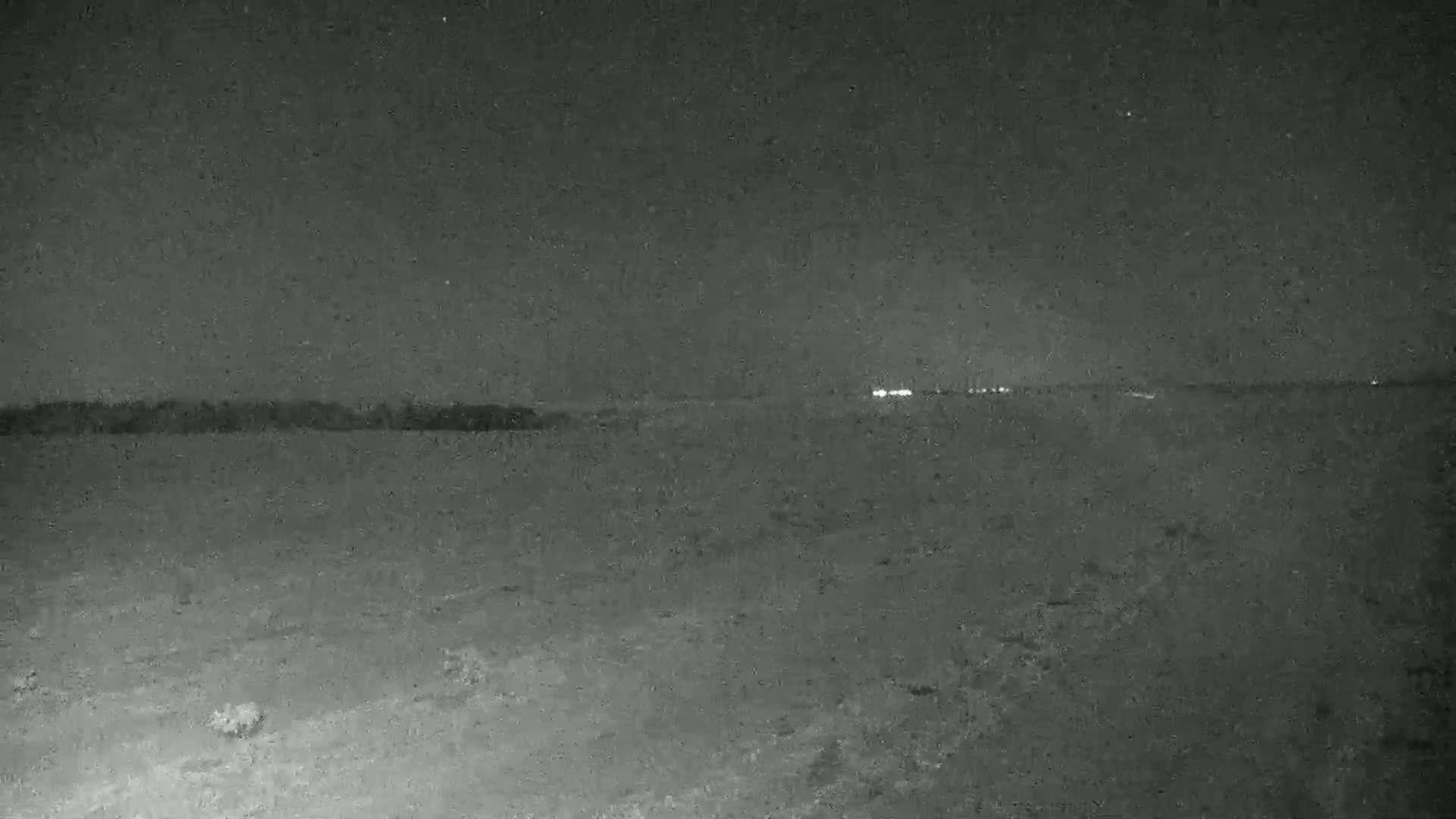 A dark, flat landscape is visible under a night sky, with a line of distant lights on the horizon.