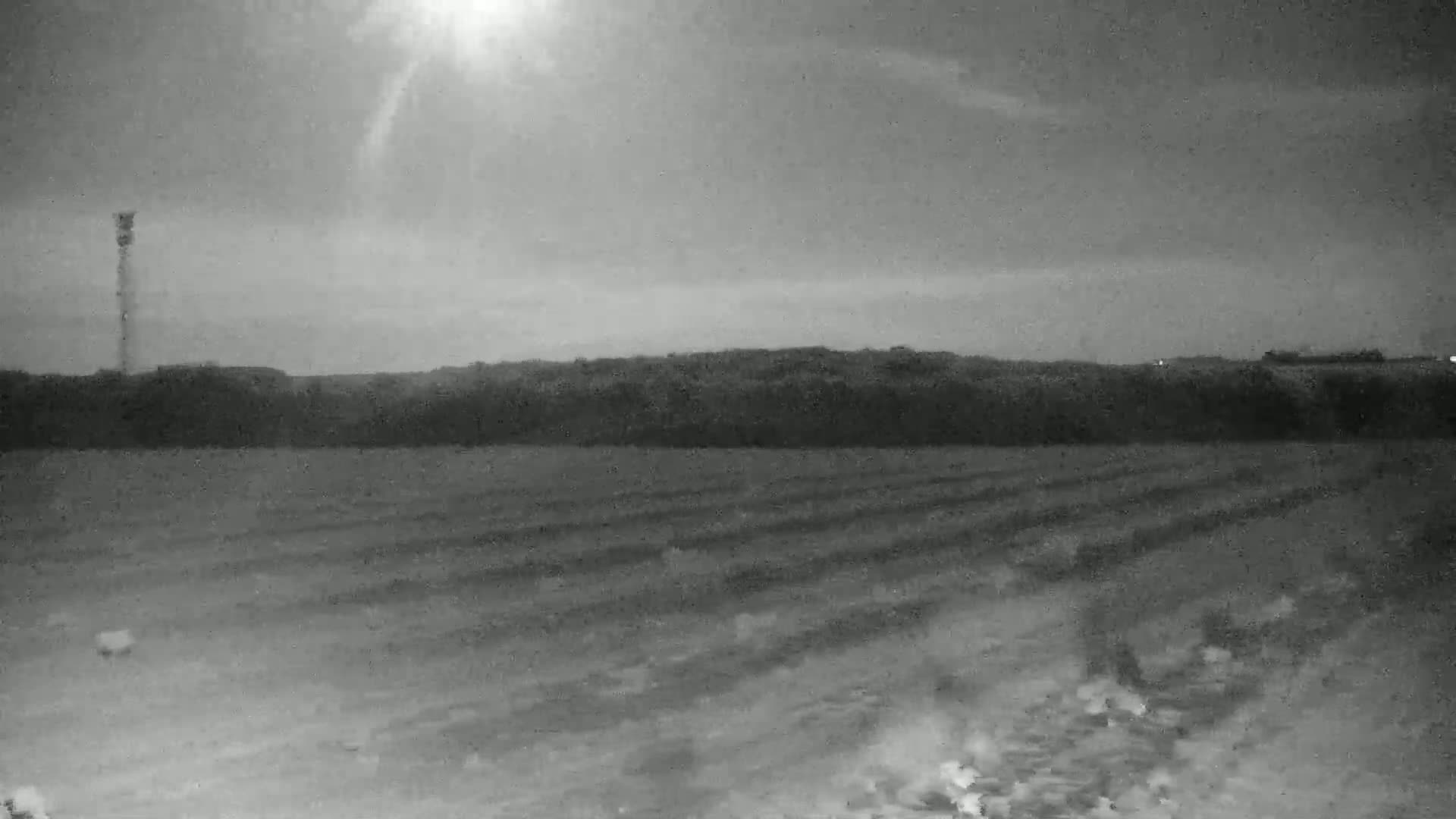 A tall tower stands in a flat, plowed field under a hazy, overcast sky.