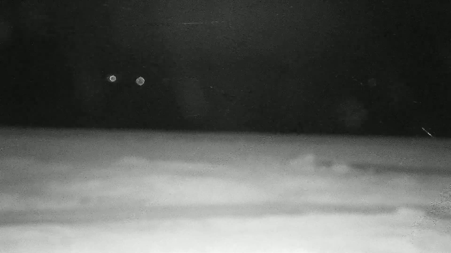 A blurry nighttime image shows two bright lights in a dark sky above a hazy, light-grey ground.