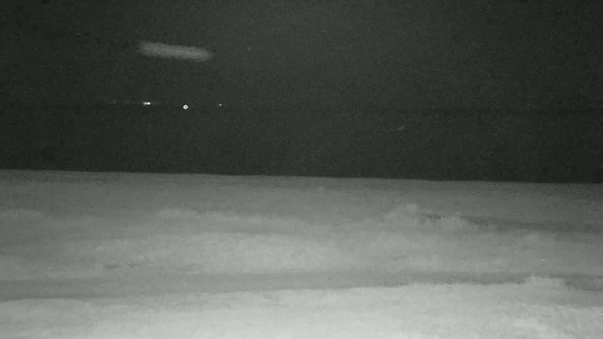 A dark, nighttime scene shows a flat, snow-covered ground under a cloudy sky.