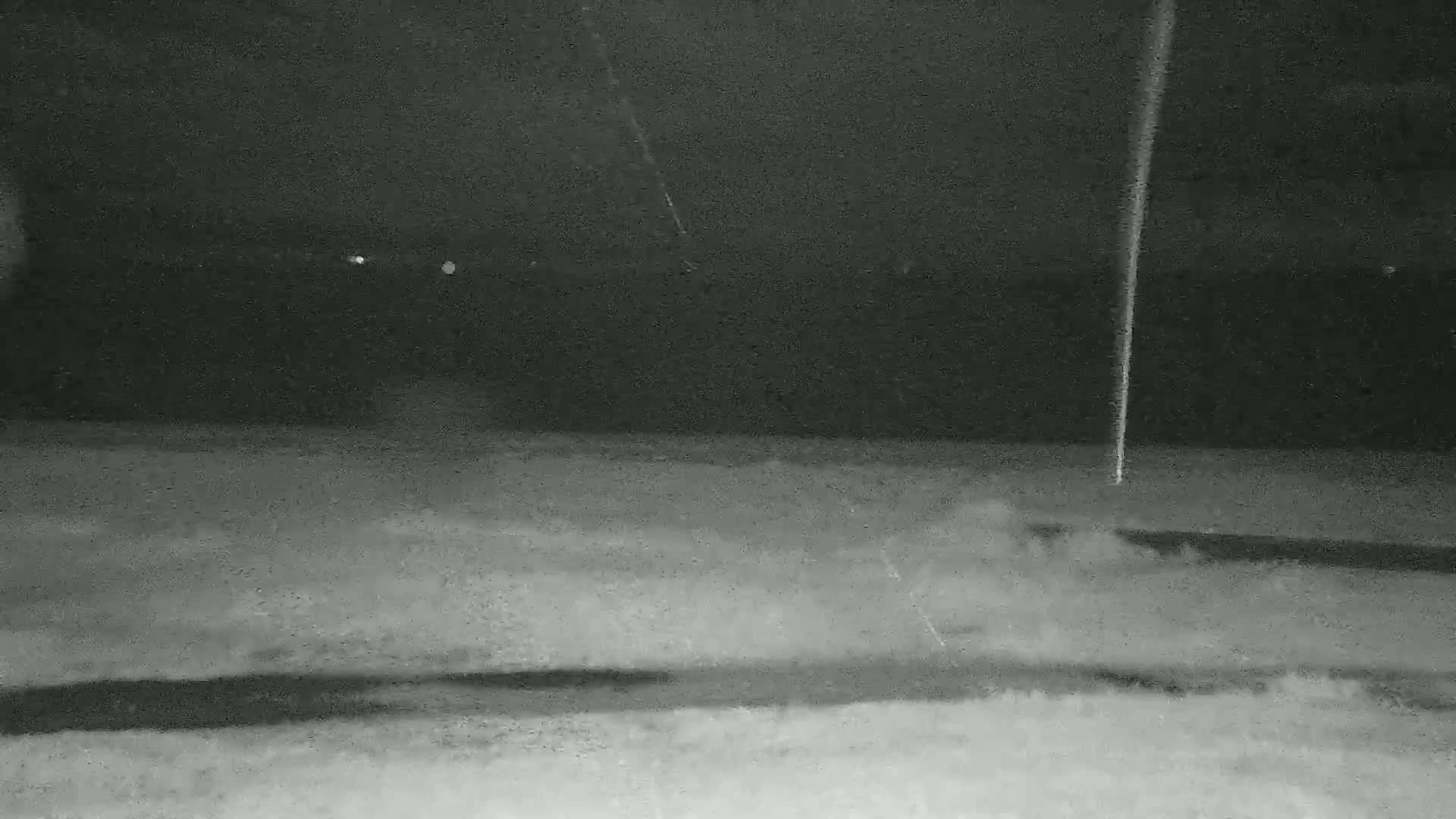 A dark, nighttime scene shows a flat, snow-covered ground with a tall, thin object standing in the distance.