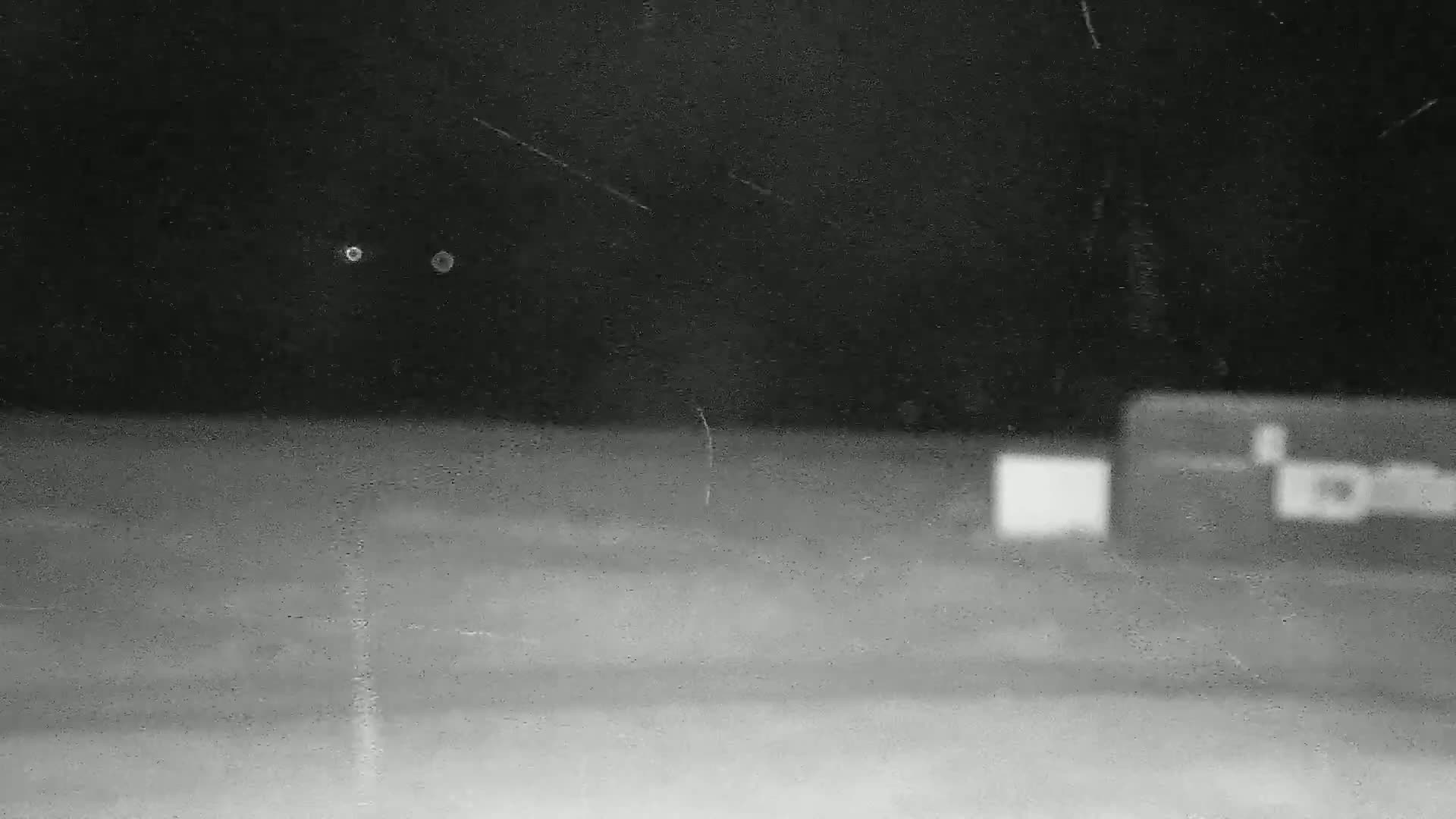 A blurry, out-of-focus nighttime image shows two small lights in the dark sky above a flat, indistinct ground with two out-of-focus rectangular objects in the lower right.