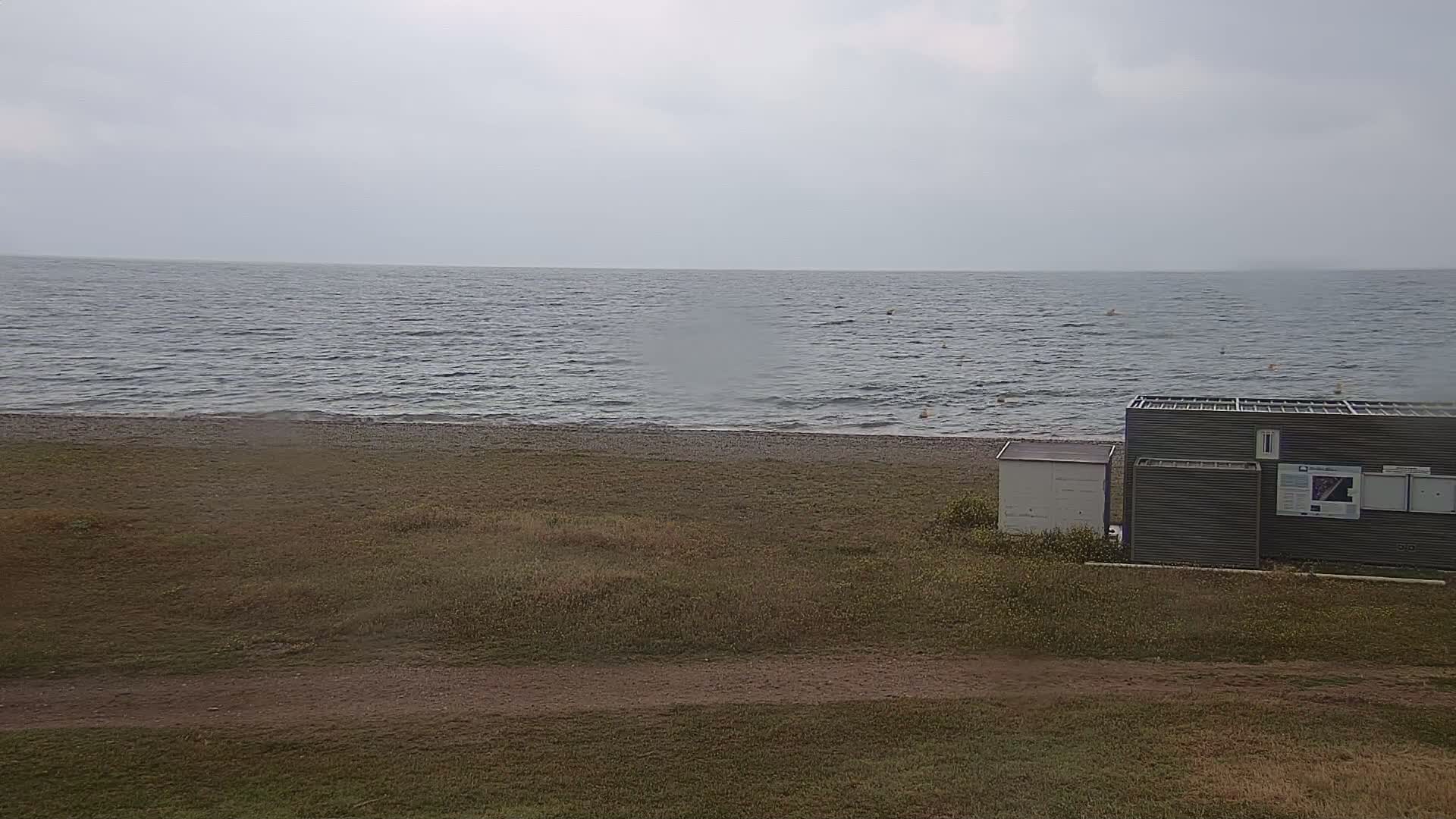 A gray building sits on a grassy area next to a beach with a choppy gray sea under an overcast sky.