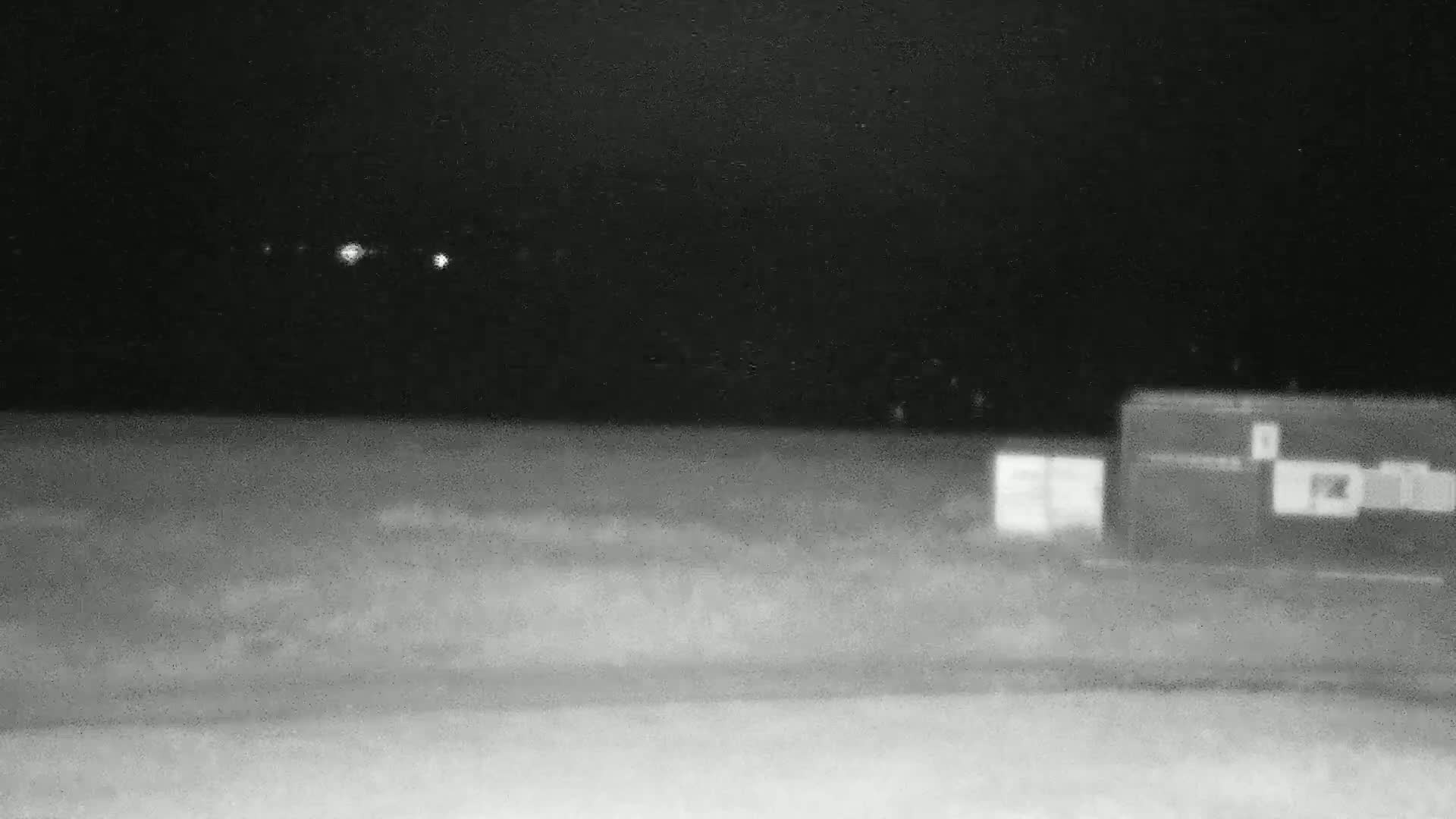Under a dark night sky, two blurry, rectangular structures sit in a flat, open space.