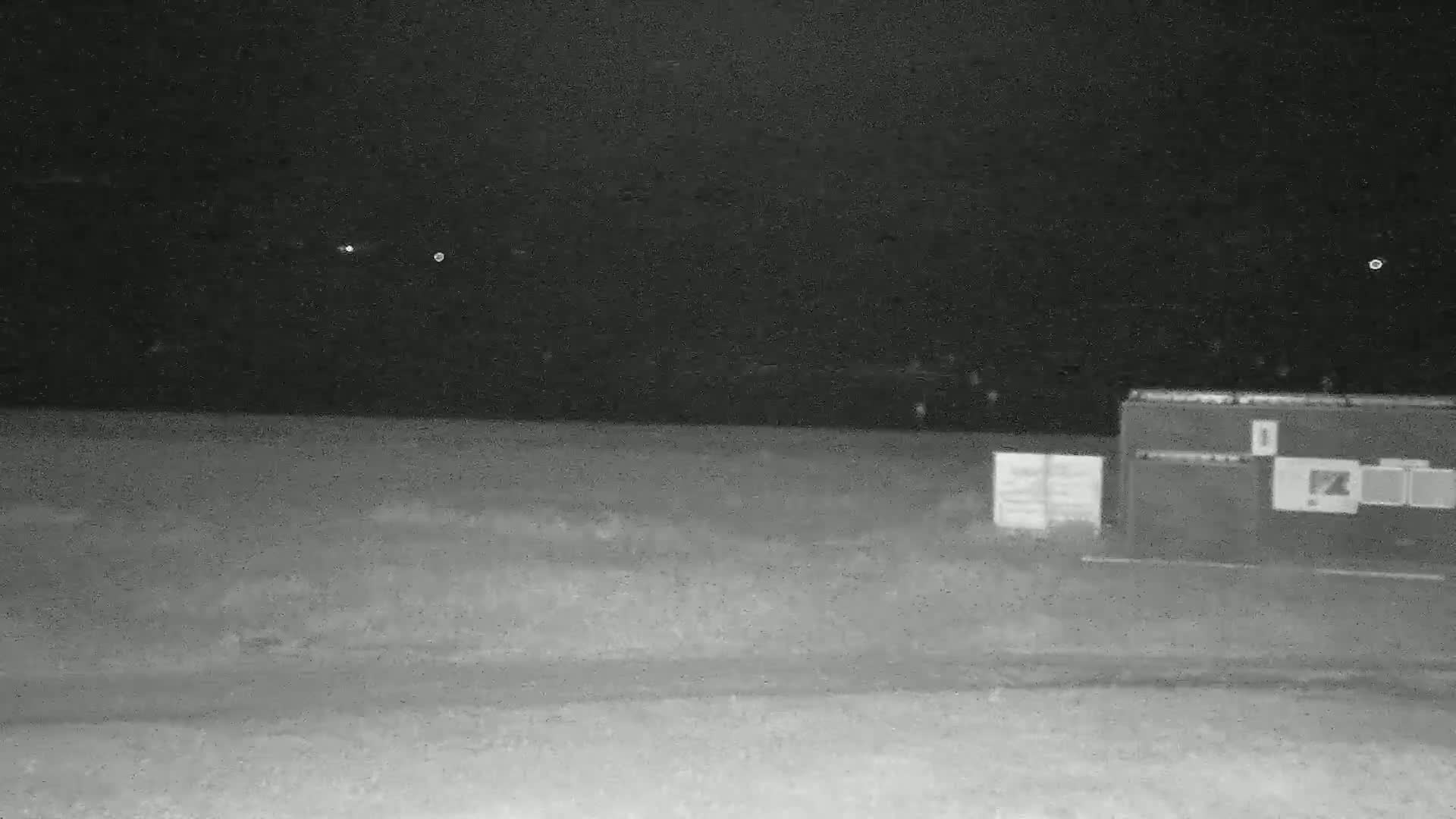 Under a dark, clear night sky, a flat, grassy area contains several structures, including a large, rectangular one with smaller ones beside it.