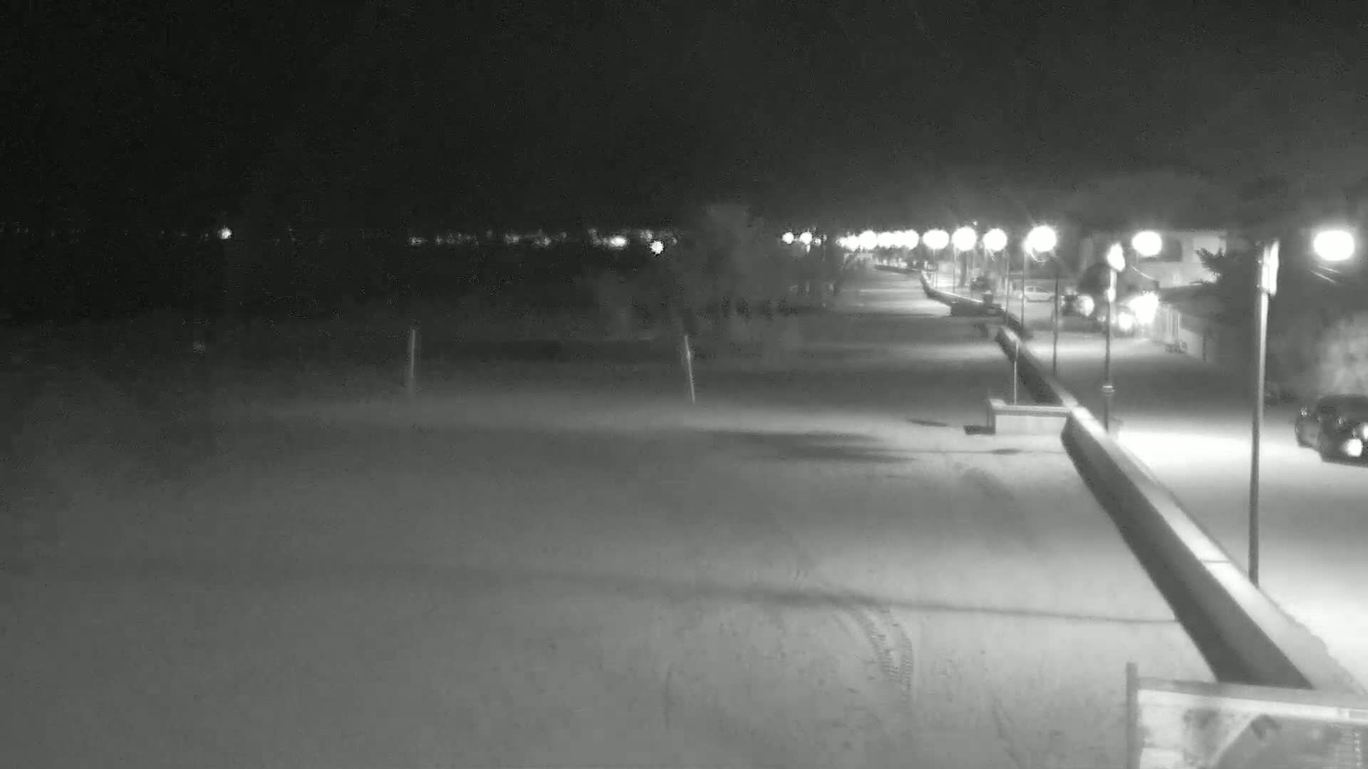 A snow-covered beach at night is illuminated by a line of streetlights along a paved walkway.