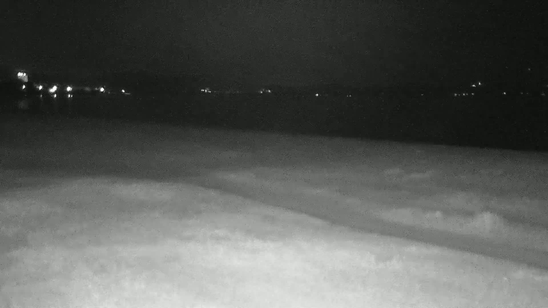 A nighttime view of a dark body of water with a distant shoreline featuring faint lights, under a clear, dark sky.