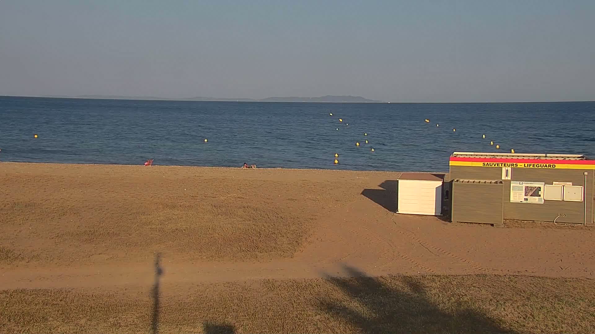 A sandy beach with a few people and a lifeguard station is visible, overlooking a calm sea on a clear day.