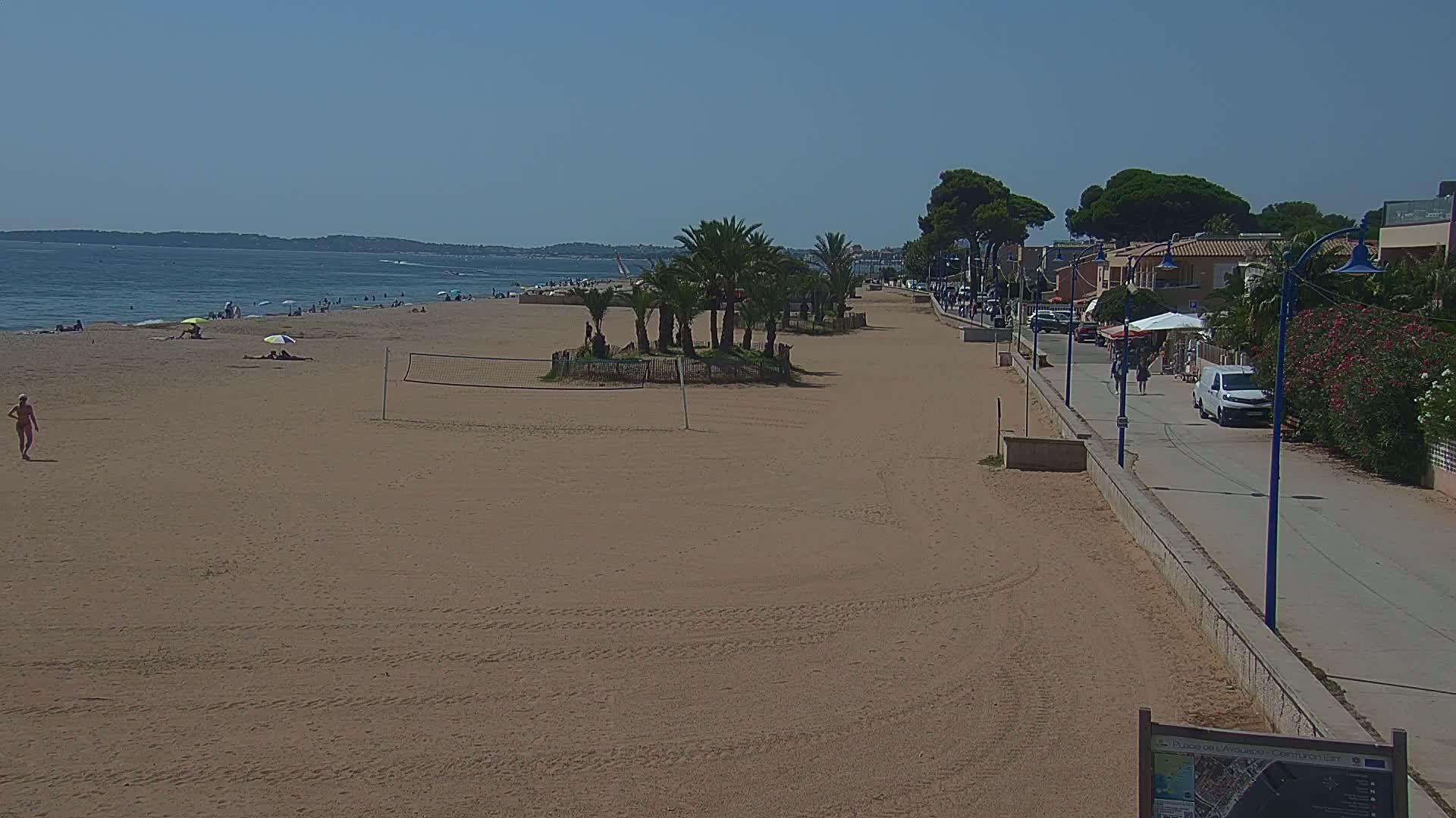 A sandy beach with a few people swimming and relaxing near a lifeguard station, under a clear blue sky.