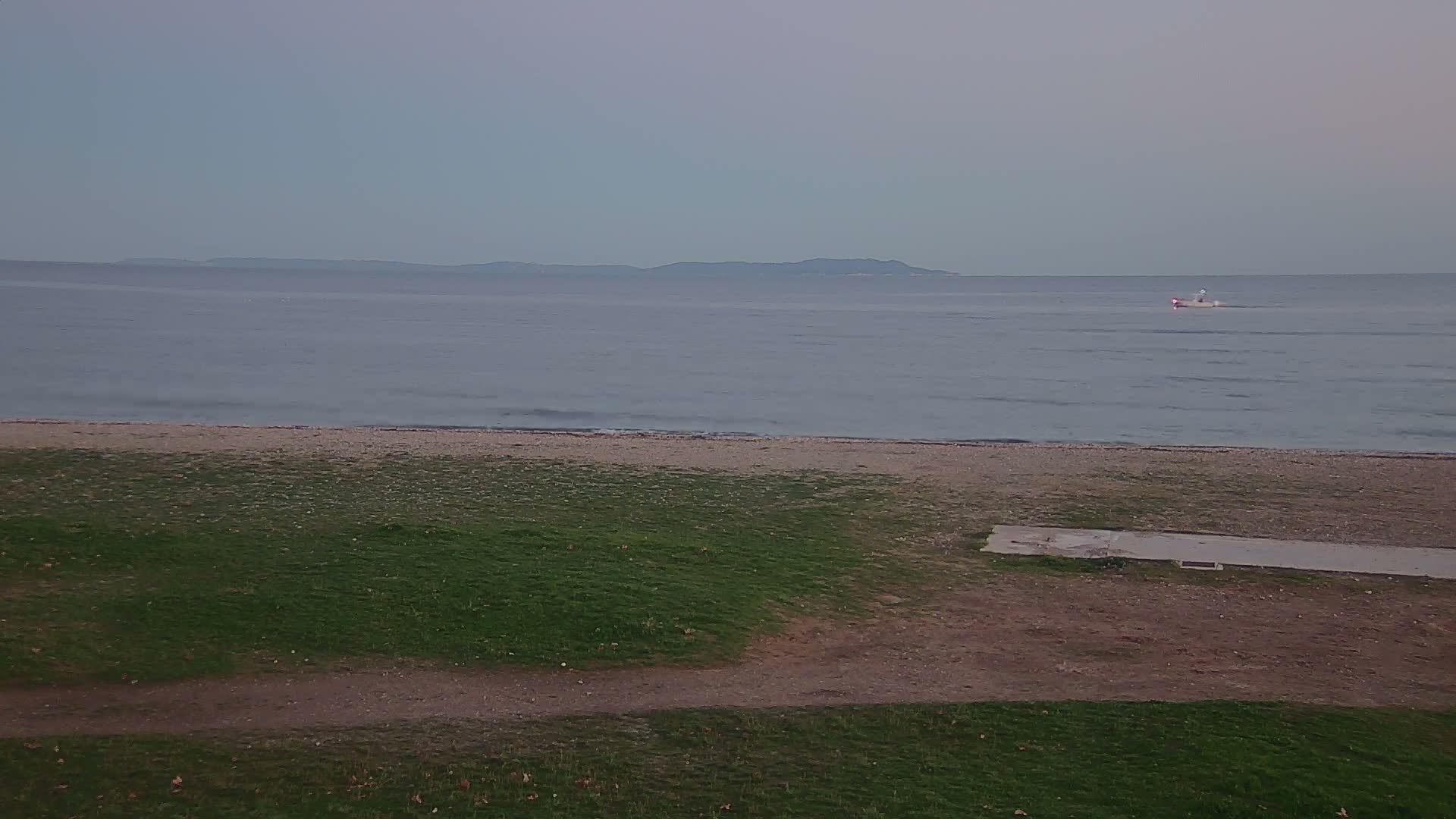 A sandy beach with a few people swimming and relaxing near a lifeguard station, under a clear blue sky.