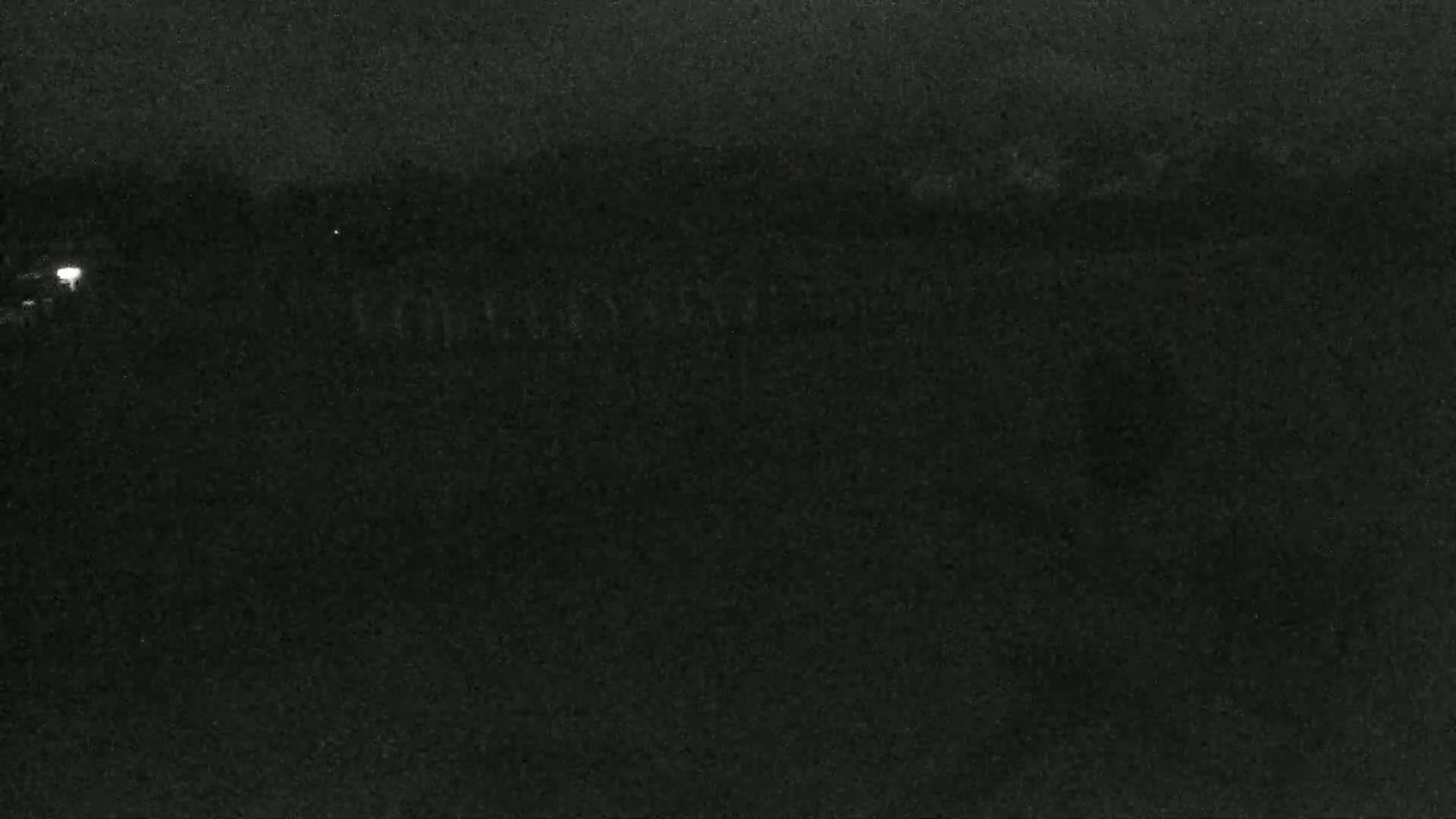 A dark, nighttime scene shows a mostly indistinct landscape under a cloudy sky.