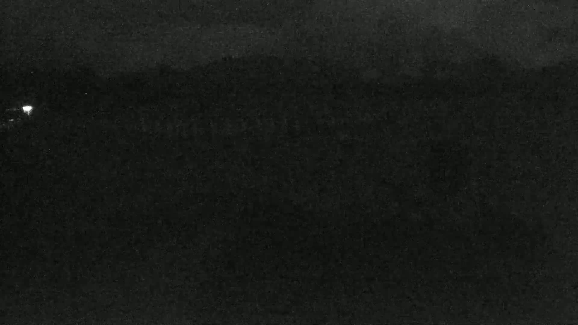 A dark, nighttime scene shows a dimly lit, flat expanse of land under a cloudy sky.