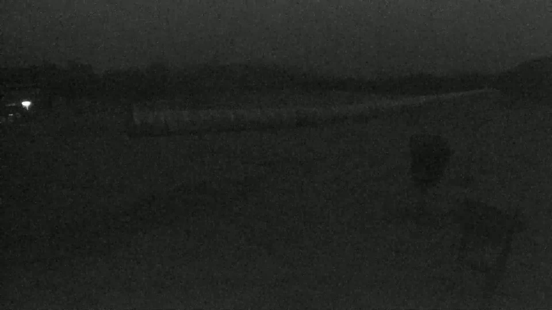 A dark, nighttime scene shows a blurry, indistinct landscape with a faint light source in the distance.