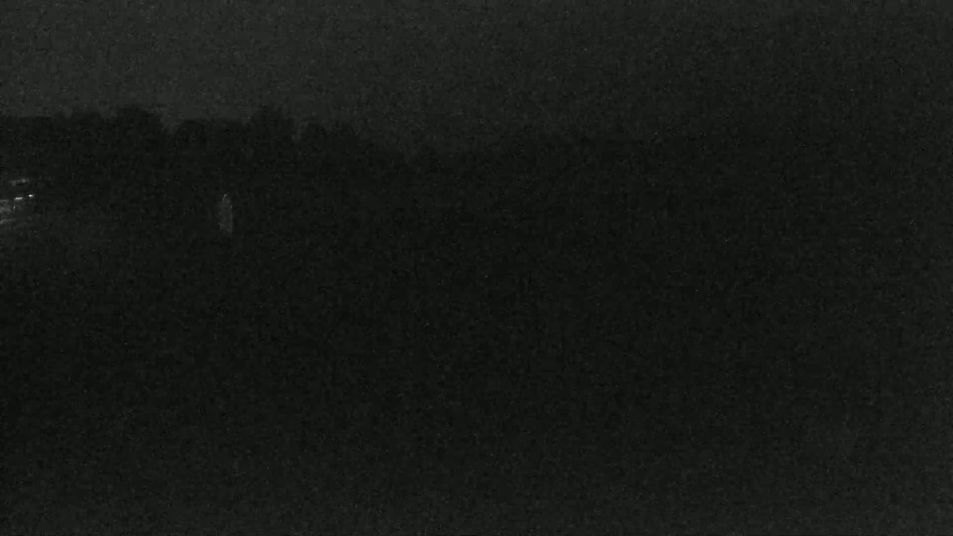 A dark, nighttime scene shows a blurry, indistinct landscape with faint lights in the distance.