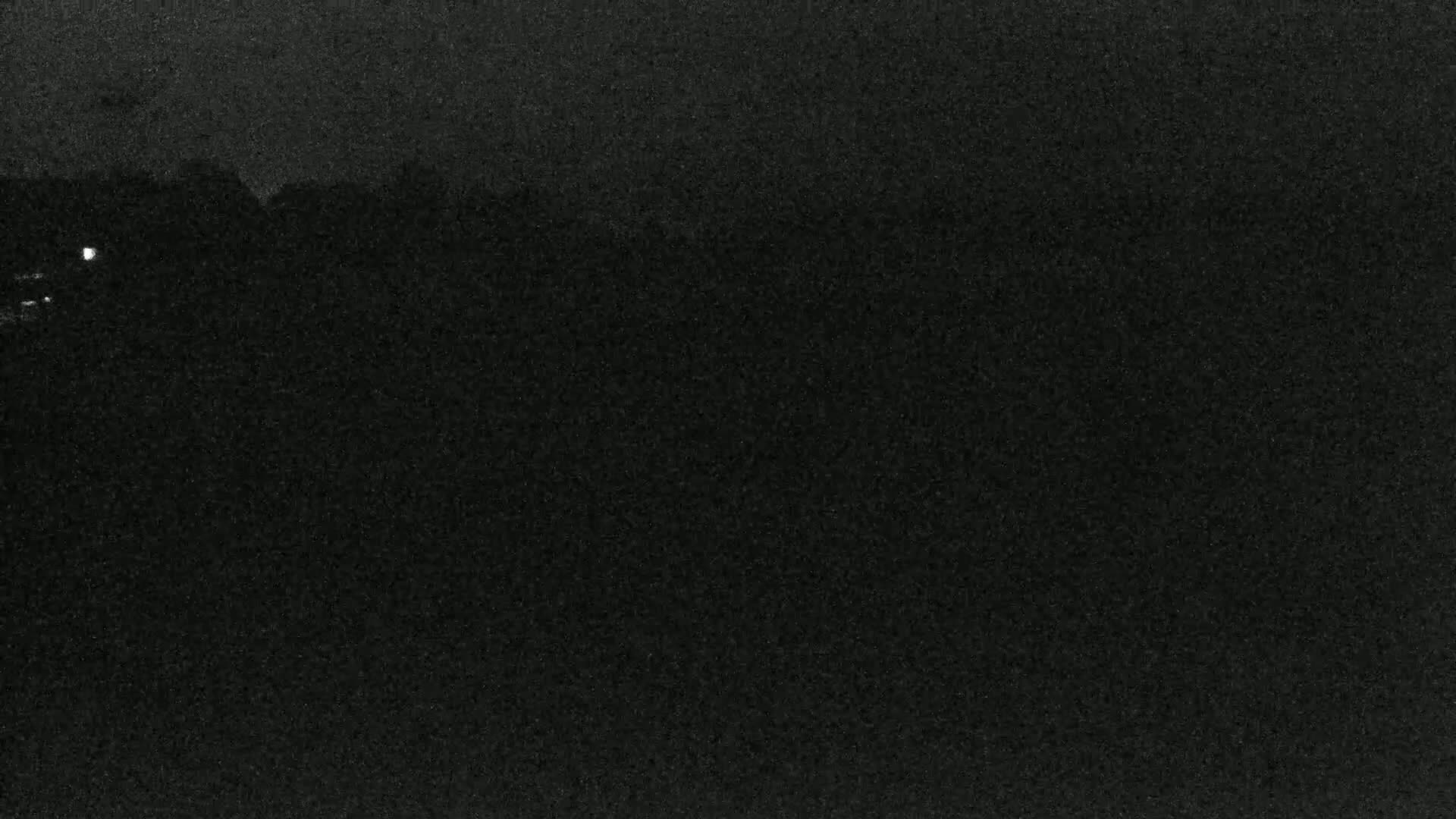 A dark, grainy image shows a mostly obscured landscape at night, with a few faint lights visible in the distance.