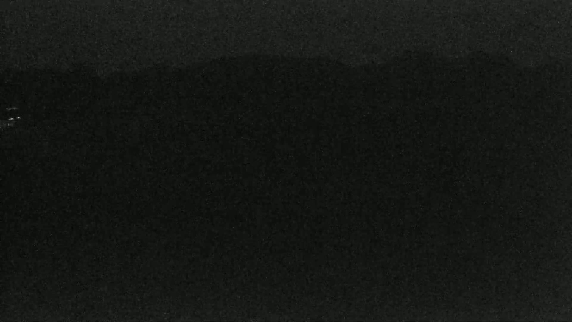 A dark, possibly nighttime, image shows a blurry, indistinct landscape with a faint suggestion of hills or mountains in the distance.