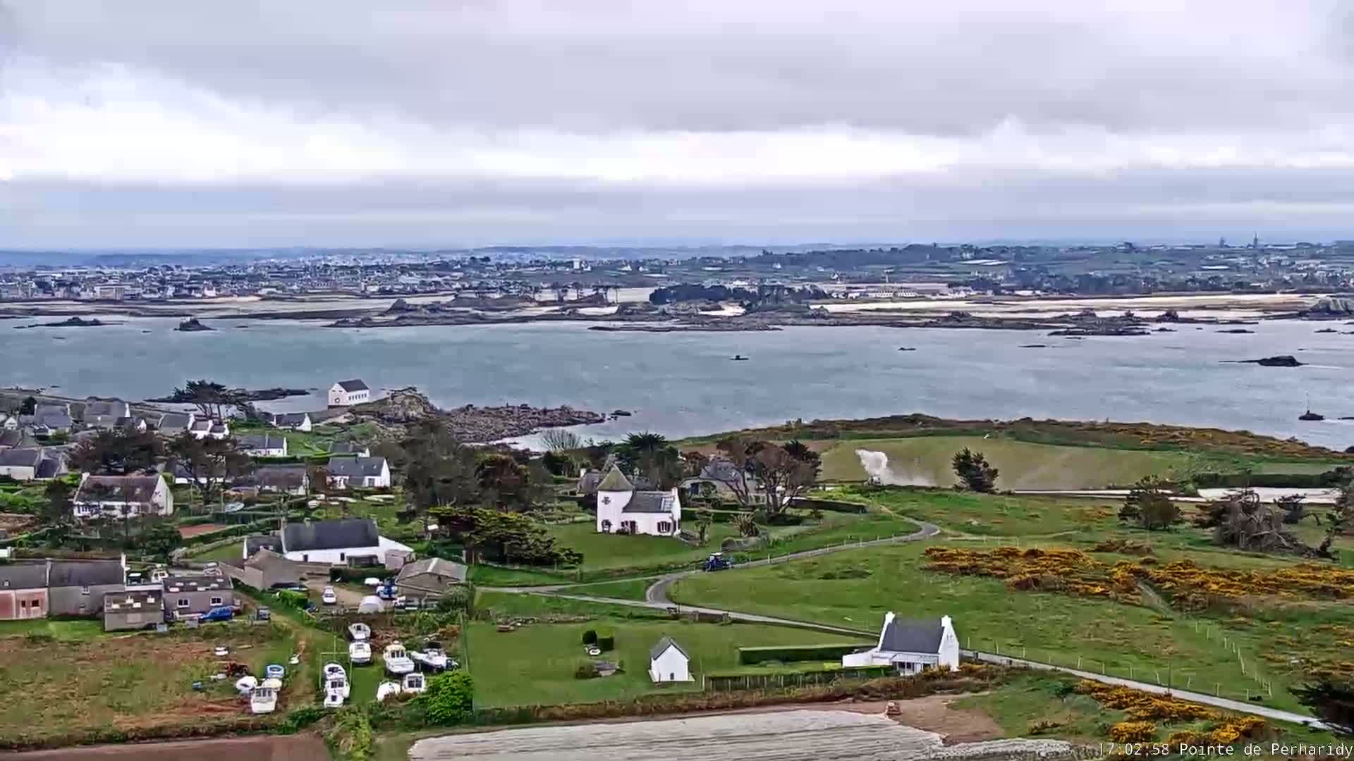 A coastal village with white buildings and boats near a body of water under an overcast sky.