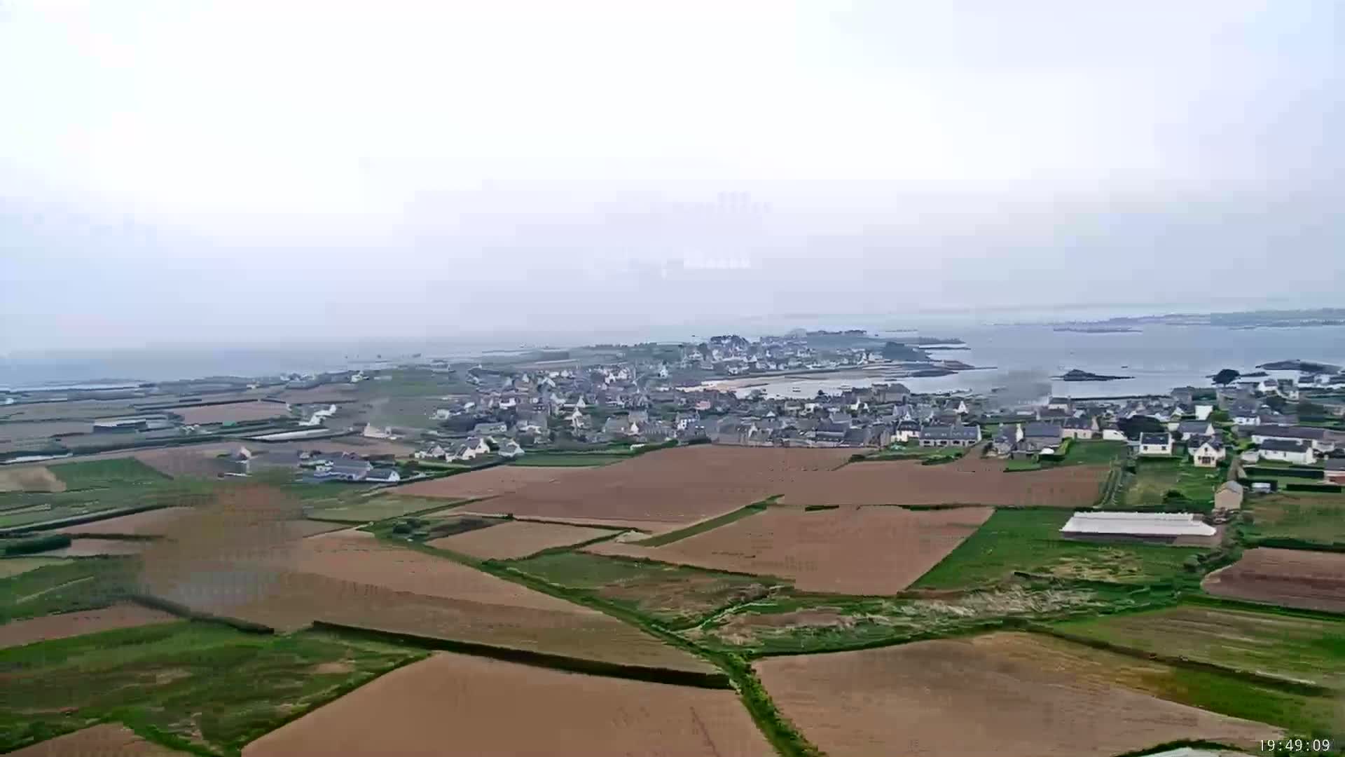 A coastal town with surrounding farmland is visible under an overcast sky.