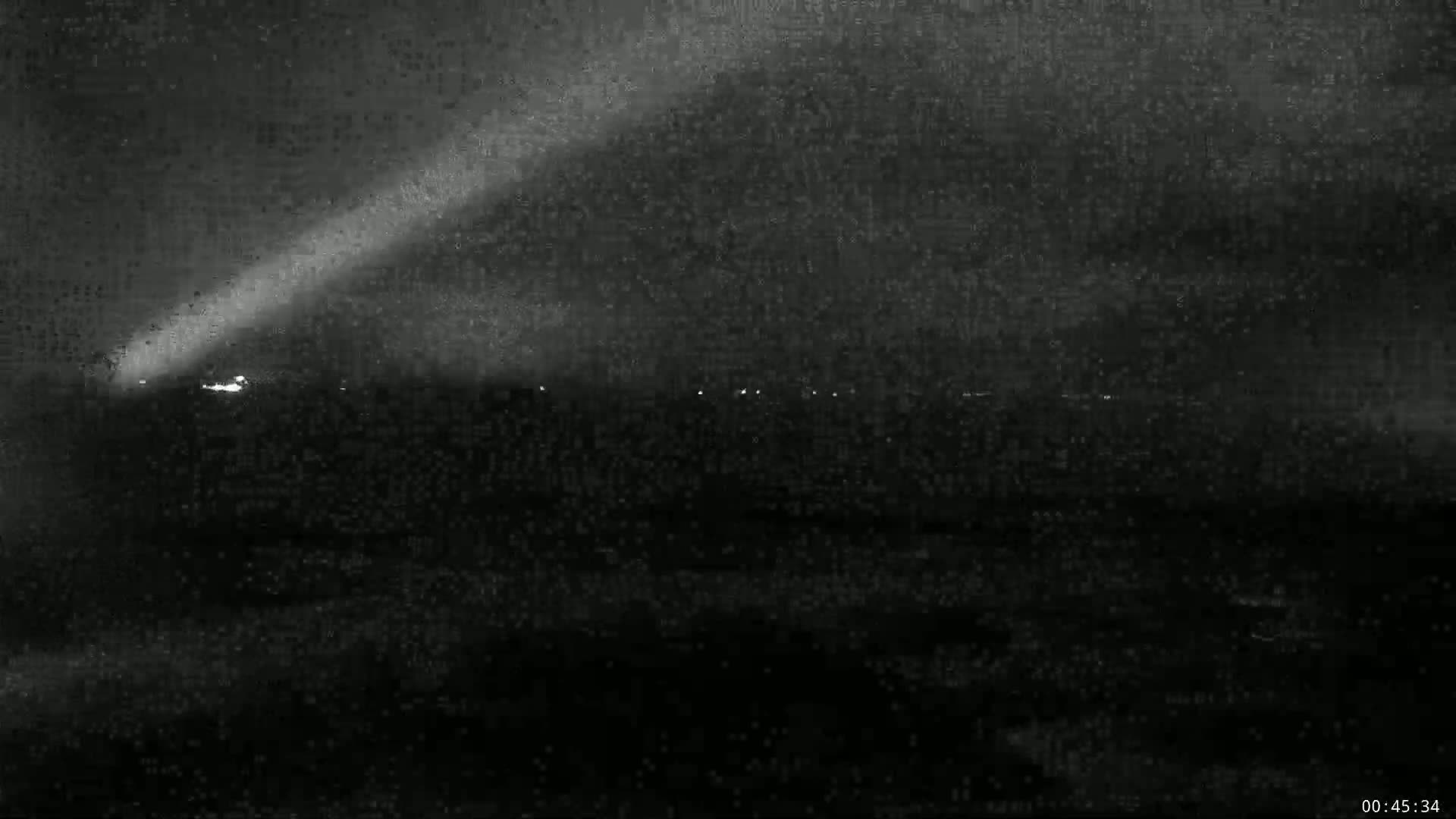A bright comet with a long tail is visible in the night sky above a dark, flat landscape with a few distant lights.