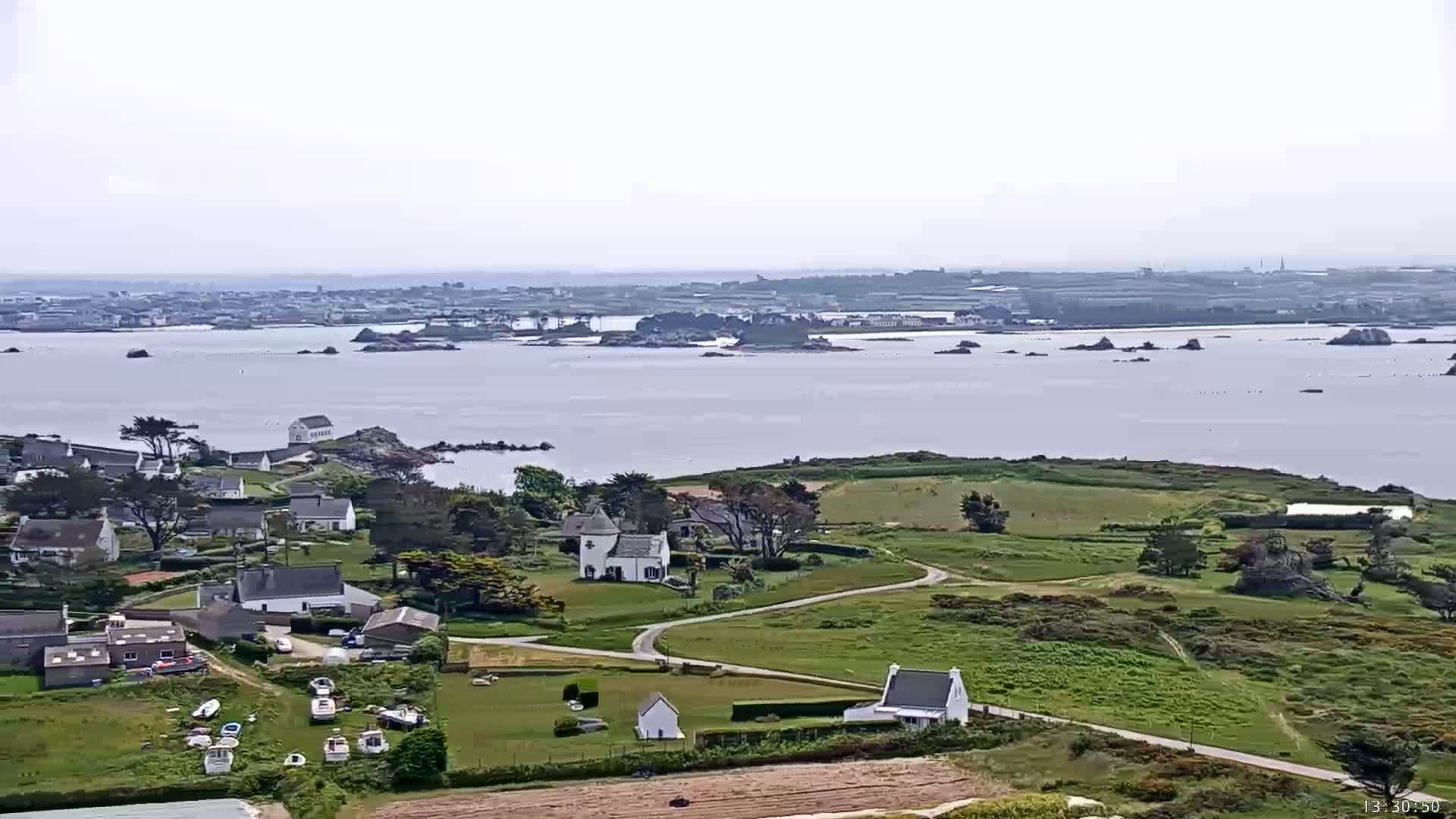 A coastal village with white houses and boats near the water is visible under a hazy sky, with islands and a larger landmass in the distance.