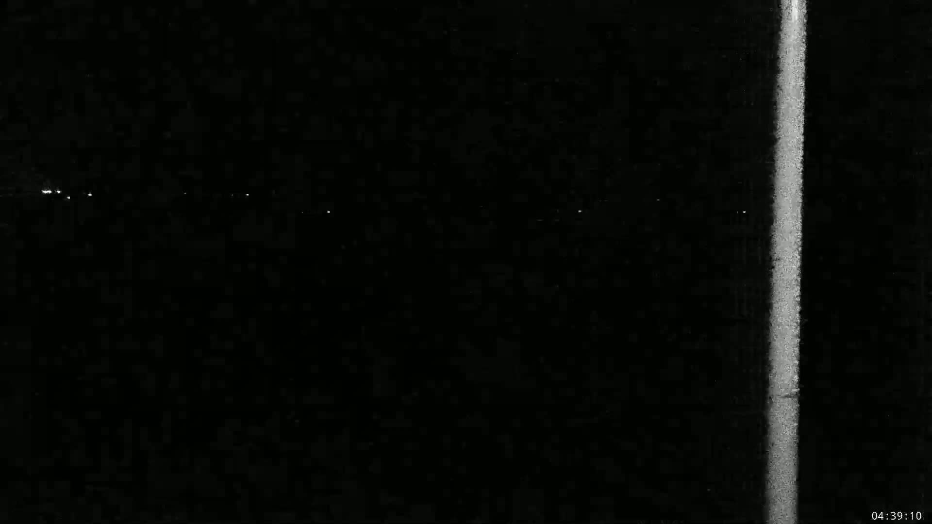 A nighttime view shows a faint line of distant lights and a bright vertical streak, likely from a camera malfunction or light source.