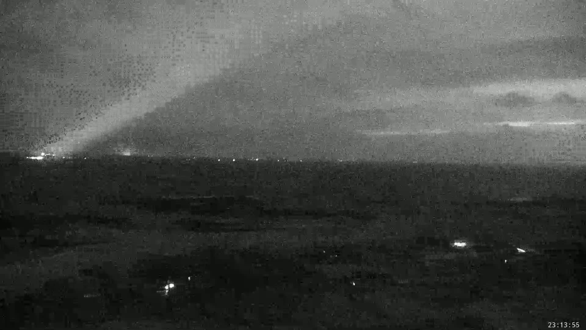A nighttime, overcast view of a distant city skyline with faint lights visible against a dark, hazy sky.