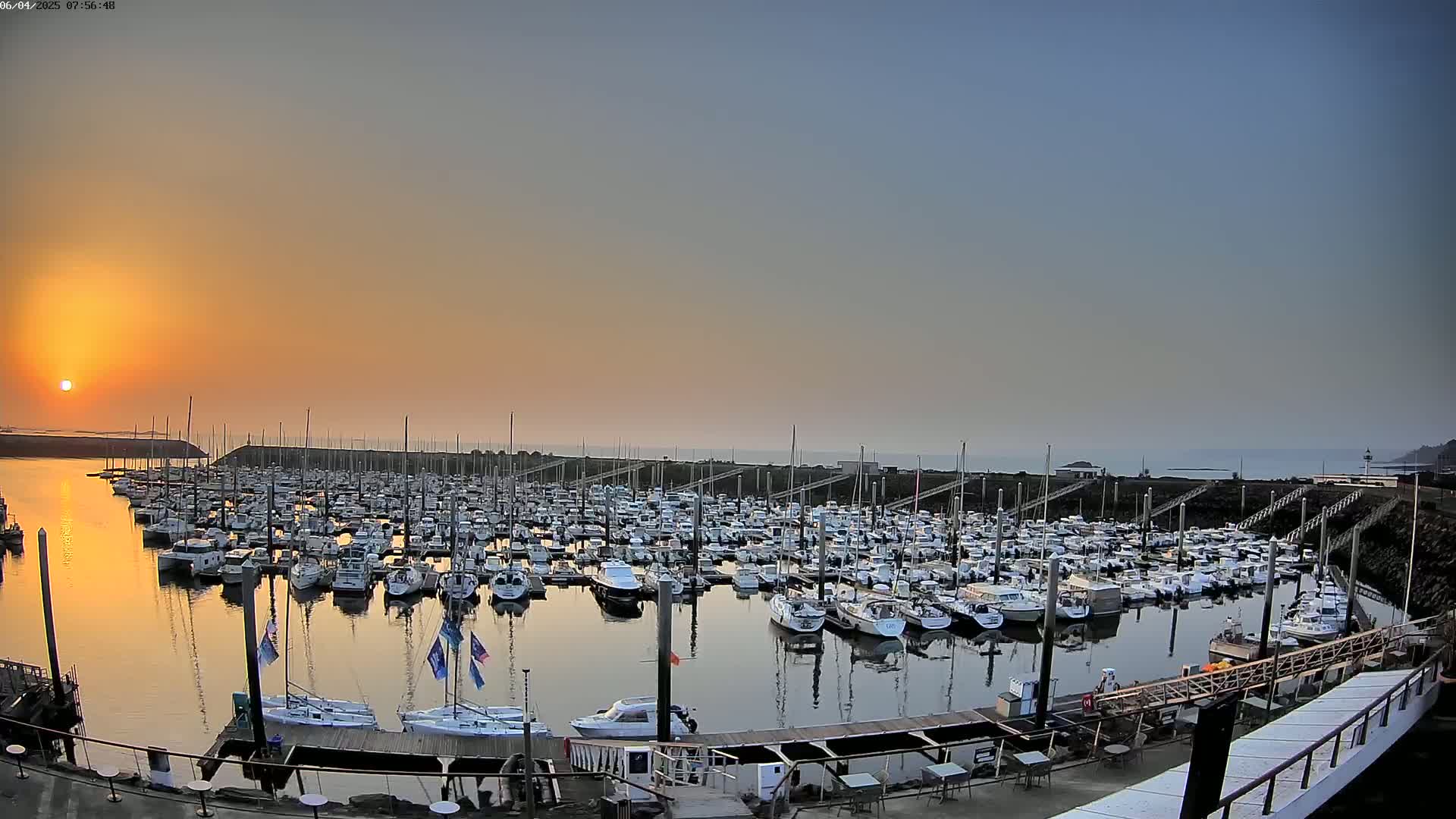 Many boats are docked in a marina at sunrise under a clear sky.