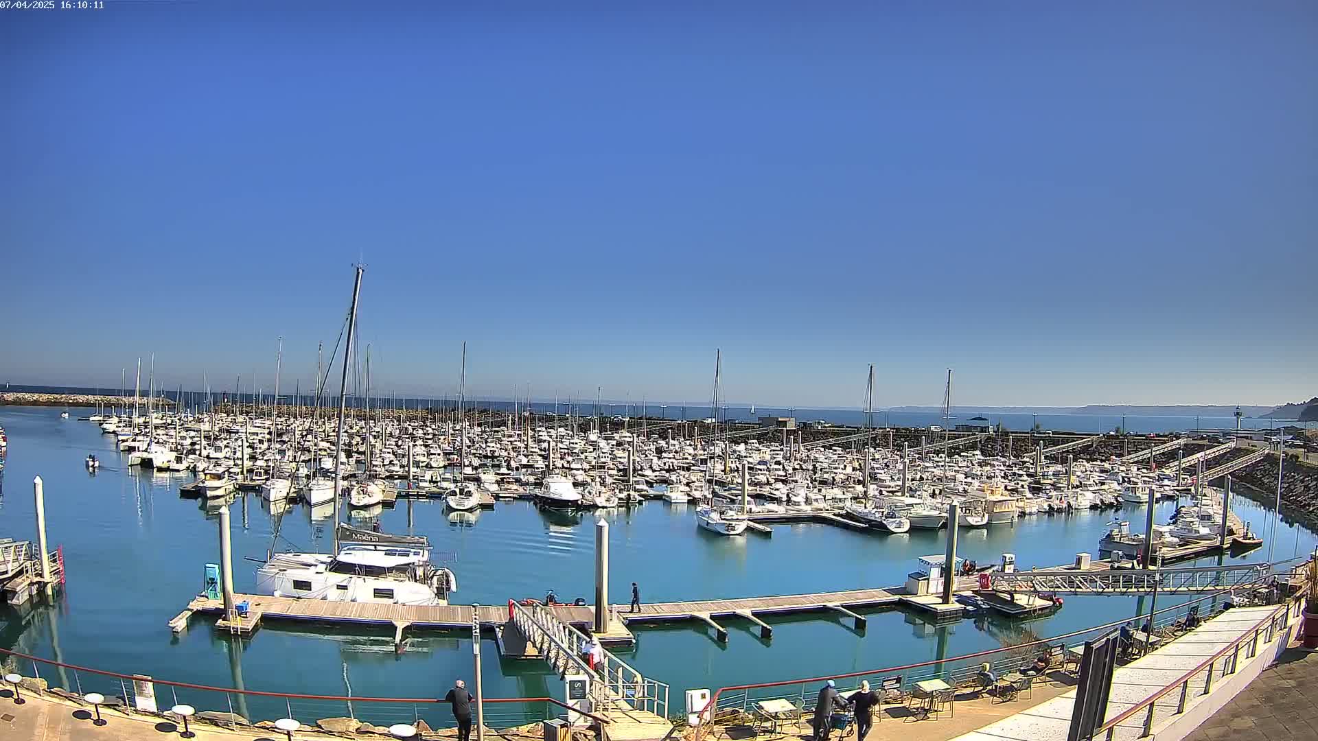 A large marina filled with numerous sailboats and motorboats under a clear blue sky.